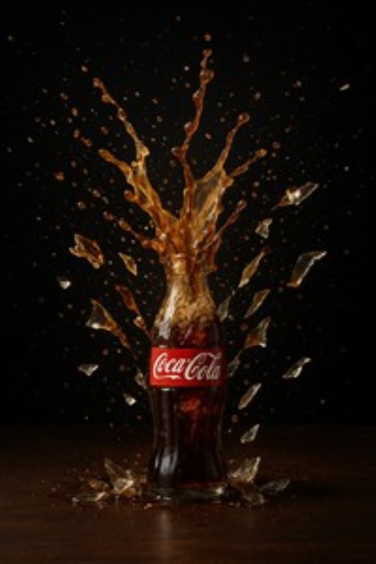 Sprudlende Coca-Cola Eksplosion - Oplev den eksotiske energi i denne fantastiske illustration af en Coca-Cola flaske, hvor sodavand sprøjter dramatisk ud mod en dyb sort baggrund. Perfekt til at tilføje liv og karakter til dit hjem.